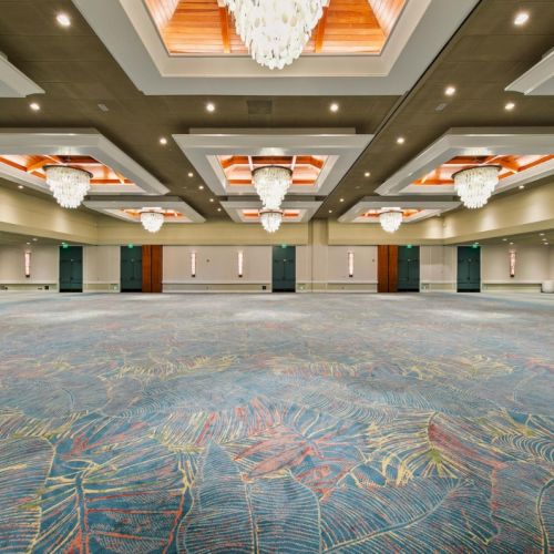 An elegant indoor event hall with patterned carpet, chandeliers, recessed lights, and tall teal-and-wood walls, ready for gatherings.