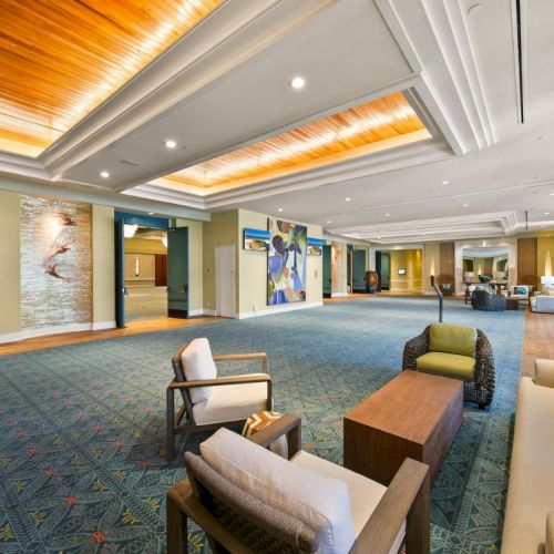A bright modern lounge or meeting room with green patterned carpet, sofas, coffee table, and framed artwork on the walls.