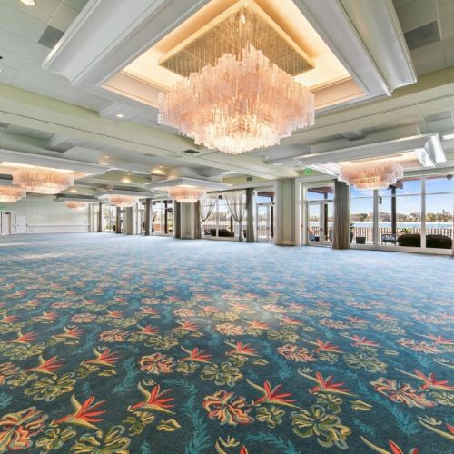 Bright ballroom interior with blue floral carpet and large crystal chandeliers near glass doors and curtains.