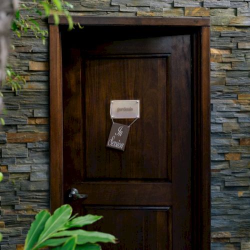 A dark wooden door set into a multicolor stone wall, with a small sign hanging near the handle.