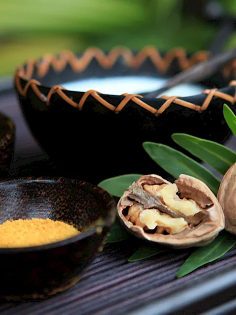 Walnuts and nut fragments, spices in bowls, and green leaves on a dark wooden tray.