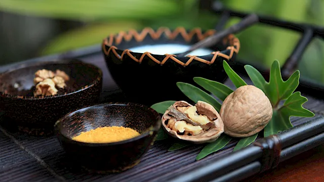 Walnuts and nut fragments, spices in bowls, and green leaves on a dark wooden tray.