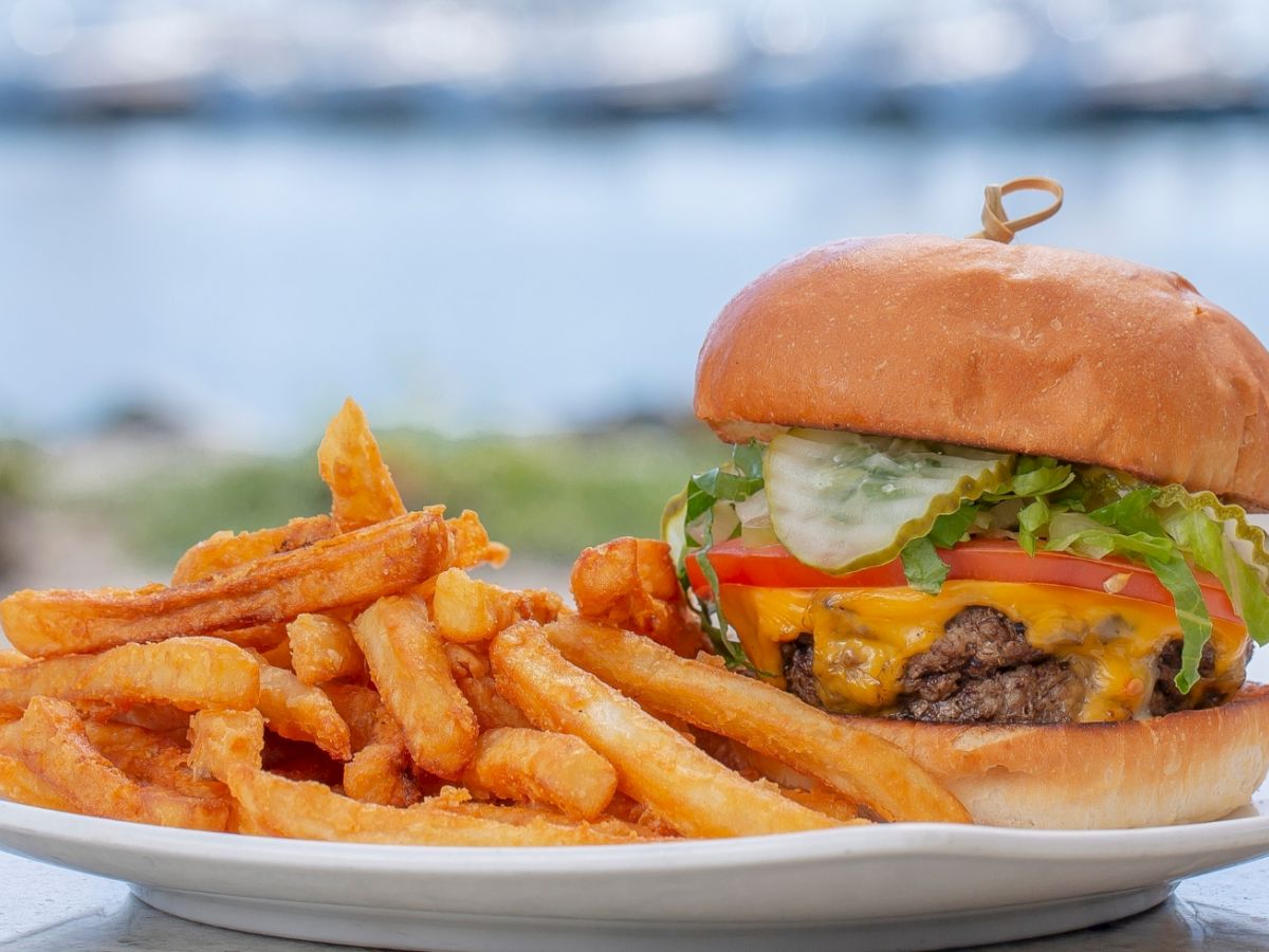 A juicy cheeseburger with lettuce and tomato, topped with fries on a beach table, ready to eat.