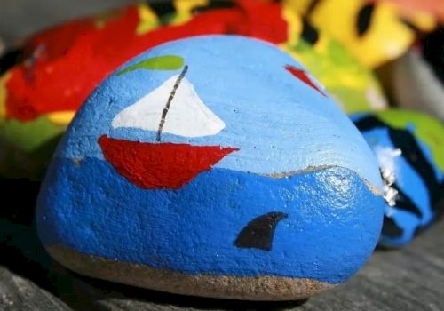 A blue stone/egg painted with a red smiling face, with other colorful toys/art pieces in the background.