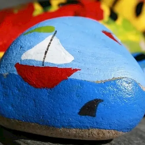 A blue stone/egg painted with a red smiling face, with other colorful toys/art pieces in the background.