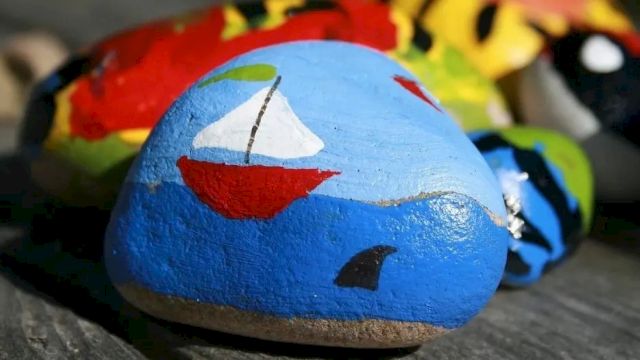 A blue stone/egg painted with a red smiling face, with other colorful toys/art pieces in the background.