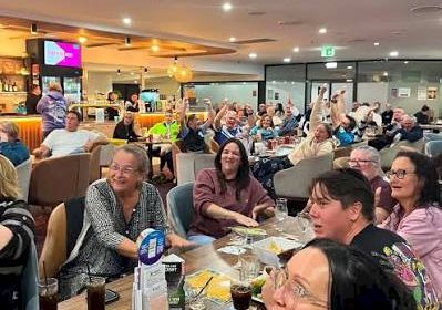 A busy restaurant with many people dining together, smiling and chatting under glowing ceiling lights.