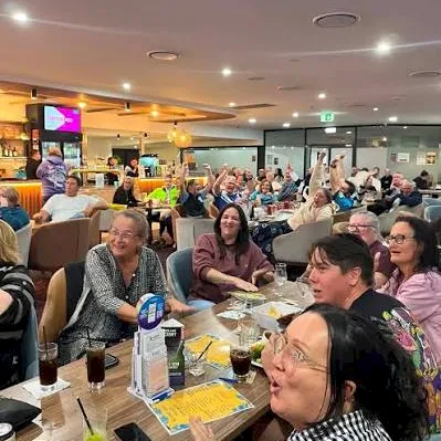 A busy restaurant with many people dining together, smiling and chatting under glowing ceiling lights.