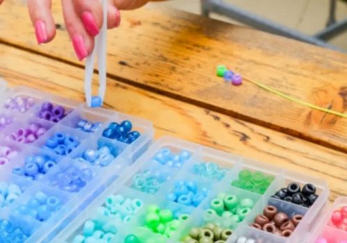A hand is arranging colorful plastic beads in small compartment containers on a wooden table.