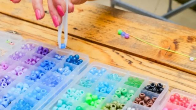 A hand is arranging colorful plastic beads in small compartment containers on a wooden table.