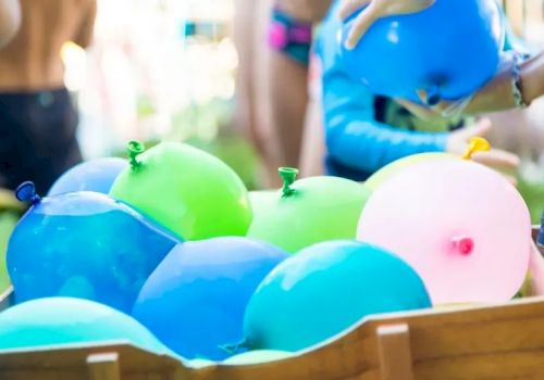Colorful balloons piled in a wooden crate at a kids&rsquo; party, with children in the background.