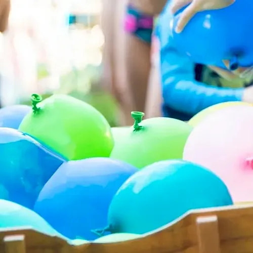 Colorful balloons piled in a wooden crate at a kids&rsquo; party, with children in the background.