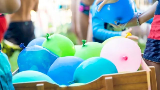 Colorful balloons piled in a wooden crate at a kids&rsquo; party, with children in the background.
