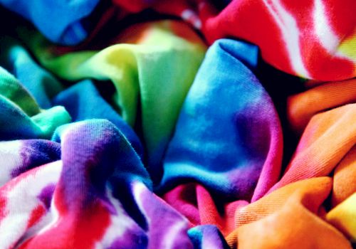 Colorful folded fabrics and clothes fill the frame, with bright reds, blues, greens, and purples.