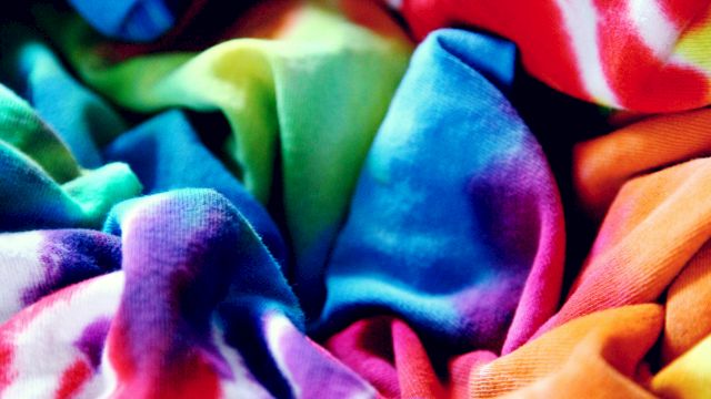 Colorful folded fabrics and clothes fill the frame, with bright reds, blues, greens, and purples.