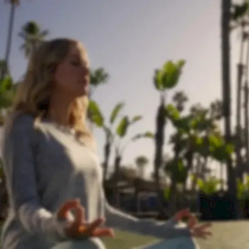 A woman in a sunny park stretches outdoors with palm trees lining the walkway behind her.