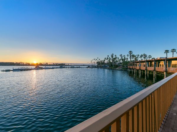 Sunset over a calm harbor with a wooden walkway, palm trees, and moored boats along the pier.
