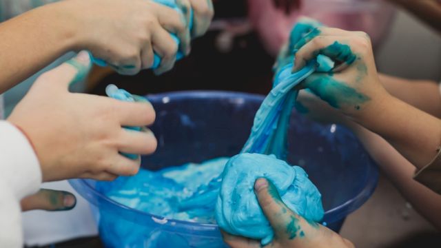A person&rsquo;s hands are covered in bright blue slime or paint, squishing and smearing it during a messy activity.