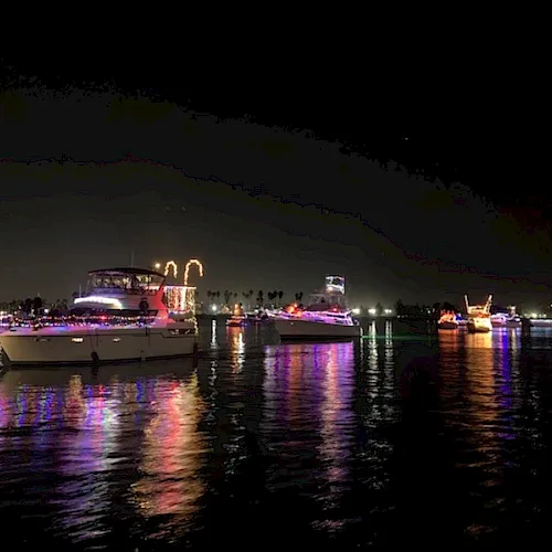 Night river harbor filled with colorful, illuminated boats and barges, their lights reflecting on calm water.